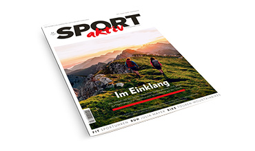 Titelbild des Magazins „Sport Aktiv“ mit zwei Personen, die bei Sonnenuntergang auf einem grasbewachsenen Bergpfad wandern. Die Überschrift lautet „Im Einklang“. Die Szene zeigt eine malerische Landschaft mit buntem Himmel und Gipfeln in der Ferne.