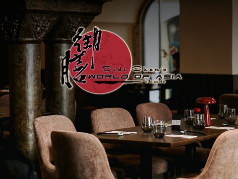 Restaurant-Innenraum mit dem Logo „Didi Chen's World of Asia à la carte“. Das Restaurant bietet einen Esstisch mit Weingläsern und sanfter Beleuchtung, umgeben von gepolsterten Stühlen und verzierten Säulen.