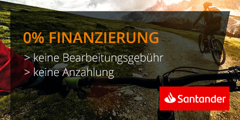 Eine Person, die bei Sonnenuntergang mit dem Mountainbike auf einem Wanderweg unterwegs ist. Im Vordergrund sind ihre Hände am Lenker zu sehen. Der Text lautet „0 % Finanzierung, keine Bearbeitungsgebühr, keine Anzahlung“ mit dem Santander-Logo in der Ecke.