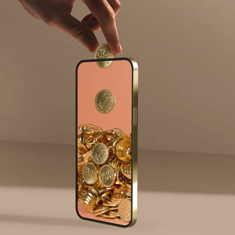 Eine Hand schwebt über einem Smartphone mit hohler Mitte und lässt eine Goldmünze hineinfallen. Das Telefon scheint vor einem braunen, minimalistischen Hintergrund mit ähnlichen Münzen gefüllt zu sein.