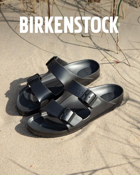 Eine Person in beigen Birkenstock-Sandalen steht neben einem Wasserspiel in einer üppigen Gartenlandschaft. Der Bereich ist von Grün umgeben und das Wort „BIRKENSTOCK“ ist deutlich über dem Bild zu sehen.