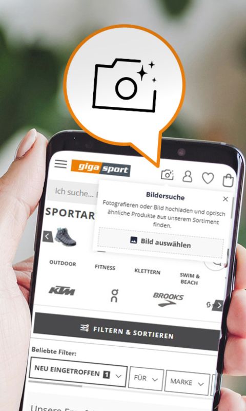 Eine Hand hält ein Smartphone, auf dem eine Sportartikel-Website angezeigt wird, mit Fahrradempfehlungen, Filteroptionen und einem Symbol, das darauf hinweist, dass Nutzer Fotos hochladen können, um nach ähnlichen Produkten zu suchen.