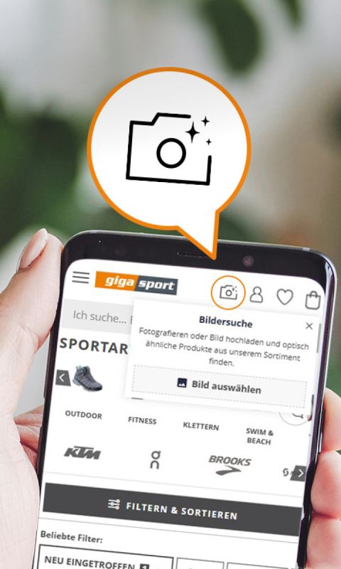Eine Hand hält ein Smartphone, auf dem eine Sportartikel-Website angezeigt wird, mit Fahrradempfehlungen, Filteroptionen und einem Symbol, das darauf hinweist, dass Nutzer Fotos hochladen können, um nach ähnlichen Produkten zu suchen.