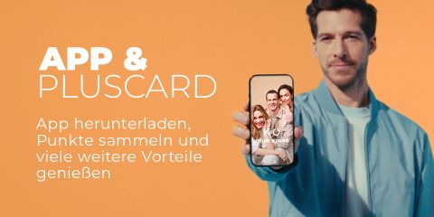 Ein Mann in hellblauer Jacke hält ein Smartphone hoch, auf dem eine lächelnde Gruppe abgebildet ist. Deutscher Text wirbt dafür, eine App herunterzuladen und mit der PlusCard Punkte für weitere Vorteile zu sammeln. Der Hintergrund ist pfirsichfarben.