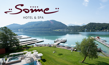 Ein Hotel und Spa am Seeufer mit Pier, Sonnenliegen, üppigem grünen Rasen und Bergen im Hintergrund unter einem strahlend blauen Himmel. Oben links ist das Logo „Some Hotel & Spa“ zu sehen.