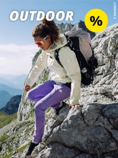 Eine Person in weißer Jacke, violetter Hose und Sonnenbrille klettert mit einem Rucksack über felsiges Gelände in den Bergen. In der oberen linken Ecke sind der Schriftzug „OUTDOOR“ und ein gelbes Prozentzeichen zu sehen.