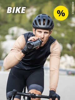 Ein Radfahrer mit Helm und Sportkleidung trinkt aus einer Flasche, während er im Freien Rad fährt. In der oberen linken Ecke erscheinen das Wort „BIKE“ und ein gelbes Prozentzeichen.