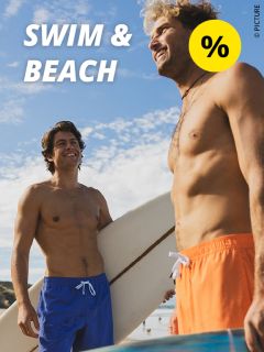 Zwei lächelnde Männer in Badehosen stehen mit einem Surfbrett am Strand. Der Himmel ist blau und bewölkt. Der Text lautet „SCHWIMMEN & STRAND“ mit einem gelben Prozentsymbol in der Ecke.