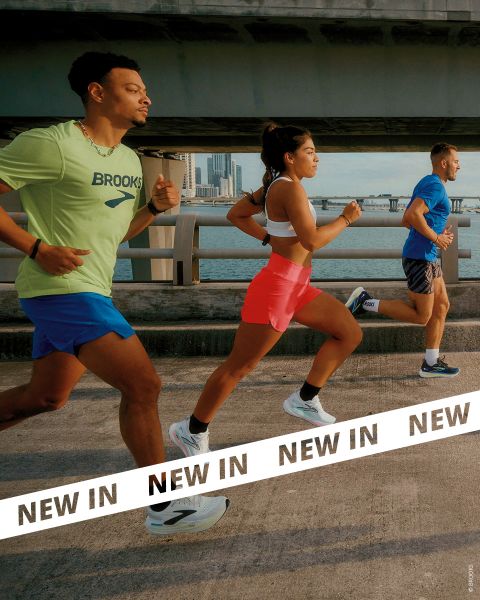 Drei Personen in Sportkleidung joggen gemeinsam im Freien auf einem Betonweg am Wasser, mit einer Brücke und der Skyline der Stadt im Hintergrund. Ein Banner mit der Aufschrift "NEW IN" erscheint im unteren Teil des Bildes.