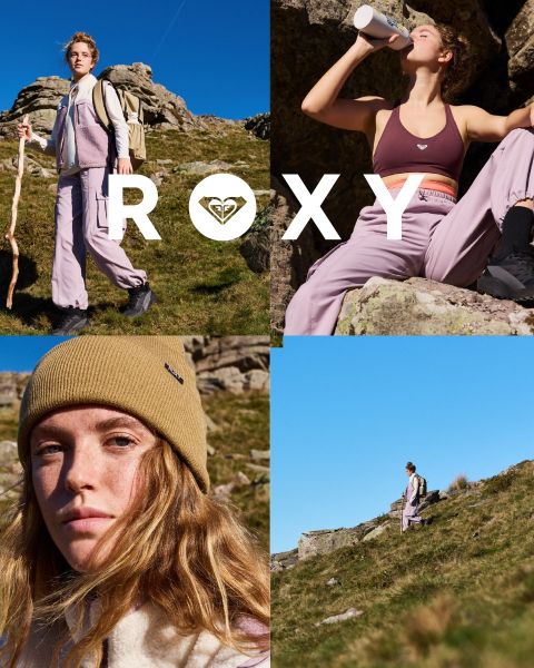 Drei Frauen schwimmen in Badeanzügen unter Wasser in klarem, blauem Wasser. Eine trägt ein Langarmshirt, die anderen Bikinis. Das Bild ist mit dem weißen „Roxy“-Logo überlagert.