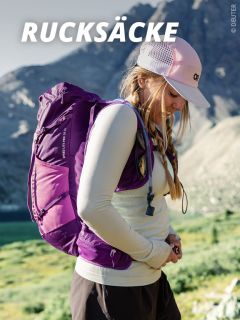 Eine Frau, die ein helles langärmeliges Hemd, eine rosa Mütze und einen lila Rucksack trägt, steht im Freien in einer bergigen Landschaft unter dem großen Text "RUCKSÄCKE.