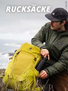 Eine Person mit dunkler Mütze und grüner Jacke sitzt im Freien, hält einen leuchtend gelben Deuter-Rucksack und steckt eine schwarze Wasserflasche in die Seitentasche. Oben steht der Schriftzug "Rucksäcke".