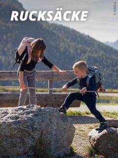 Eine Frau und ein Junge mit Rucksäcken wandern im Freien und helfen sich gegenseitig beim Klettern über Felsen, mit Bergen und Bäumen im Hintergrund. Das Wort "Rucksäcke" erscheint oben auf dem Bild.