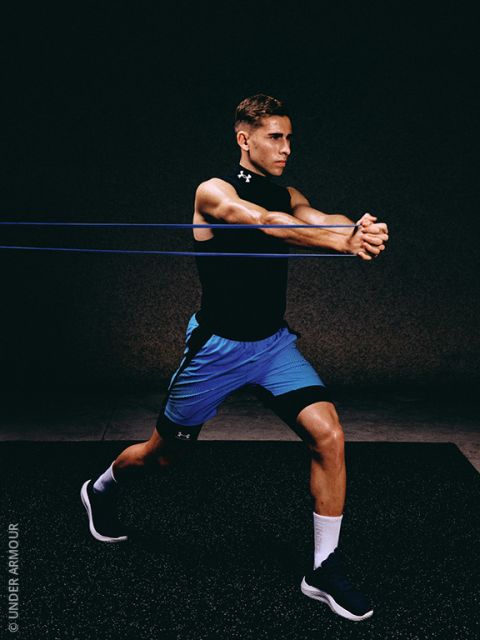 Ein Mann in Sportkleidung führt eine Widerstandsbandübung durch, indem er in einer Ausfallschrittposition steht und die Bänder mit beiden nach vorne ausgestreckten Armen vor einem dunklen Hintergrund dehnt.