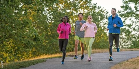 Vier Personen joggen auf einem gepflasterten Weg im Grünen. Sie tragen verschiedenfarbige Sportkleidung. Am Himmel ist der Text „LAUFSCHUH GUIDE“ zu sehen.