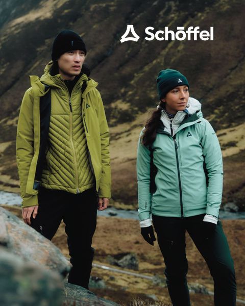 Zwei Personen in Outdoor-Ausrüstung laufen auf einem Grashügel mit Bergen und Wolken im Hintergrund. Über ihnen befindet sich das Schöffel-Logo, darunter eine dekorative grüne Wellenlinie.