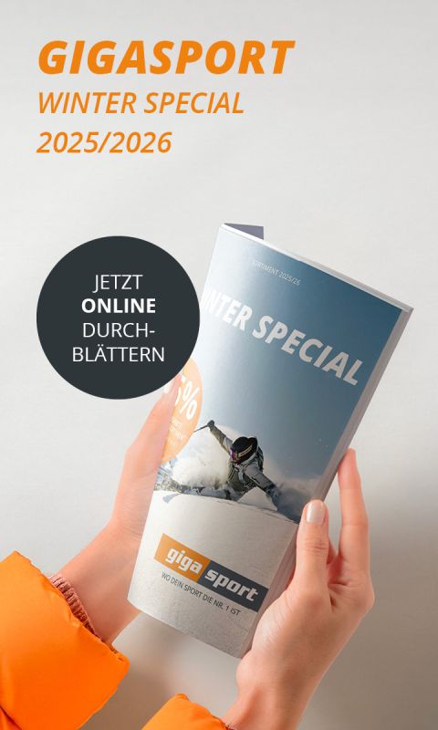 Person in orangefarbener Jacke, die eine "Gigasport Winter Special 2025/2026"-Broschüre mit einem Skifahrer auf dem Cover und einem "Jetzt online durchblättern"-Aufkleber hält.