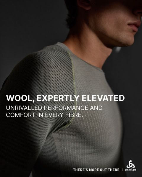 Eine Person, die ein eng anliegendes, strukturiertes, graues Wollhemd trägt, ist vom Hals bis zur Brust abgebildet. Das Bild wirbt für die hohe Leistung und den Komfort des Shirts, mit Textüberlagerung und dem Odlo-Logo in der Ecke.