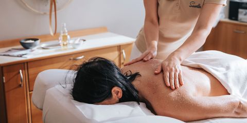 Eine Person erhält eine Rückenmassage mit Peeling in einer Spa-Umgebung; ein Massagetherapeut führt die Behandlung durch.