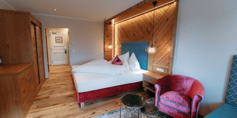 Gemütliches Hotelzimmer mit Holzboden, Doppelbett, rosa Sessel, Nachttischen und warmer Beleuchtung, mit rustikalen und modernen Dekorationselementen.