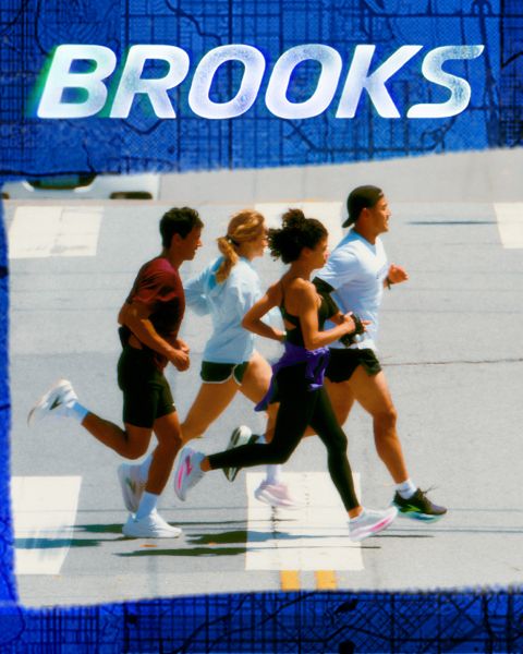 Eine Gruppe von fünf Personen rennt energisch über einen Zebrastreifen. Sie tragen farbenfrohe Sportkleidung, darunter Shorts und Tanktops. Die Szene ist lebhaft, über ihnen prangt deutlich das Wort „BROOKS“.