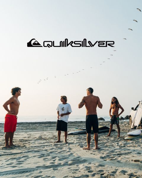 Ein Surfer reitet auf einer großen türkisfarbenen Welle und verkörpert Balance und Können. Er trägt dunkle Badeshorts, und die Welle kräuselt sich über ihm. Über ihm ist das Quiksilver-Logo zu sehen.