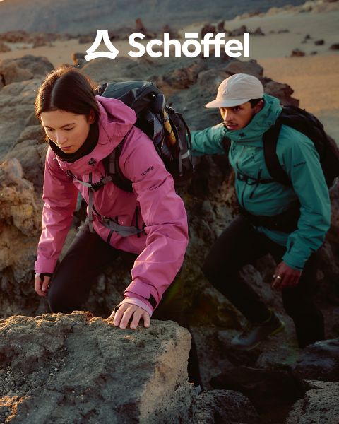 Zwei Personen in Outdoor-Ausrüstung laufen auf einem Grashügel mit Bergen und Wolken im Hintergrund. Über ihnen befindet sich das Schöffel-Logo, darunter eine dekorative grüne Wellenlinie.