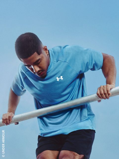 Ein Mann in einem blauen Under Armour-Hemd führt vor einem strahlend blauen Himmel eine Dip-Übung am Parallelbarren durch.