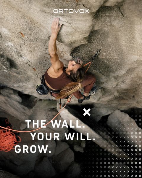 Drei Personen in Outdoor-Ausrüstung sitzen lächelnd und unterhalten sich auf felsigem Gelände in einer Bergregion. Die Sonne versinkt hinter den Gipfeln. Ein Rucksack und eine Thermoskanne stehen in der Nähe. Das Logo von Ortovox befindet sich oben rechts.