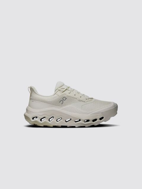 Ein grauer Sneaker mit schwarzen Details, weißer Sohle und einem markanten schwarzen „V“-Logo an der Seite. Das Wort „SNEAKER“ steht in fetter weißer Schrift oben links auf hellgrauem Hintergrund.