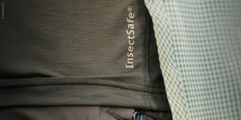 Nahaufnahme von Kleidung mit dem Text "InsectSafe®" auf einem olivgrünen Stoff neben einem grün-weiß karierten Stoff.