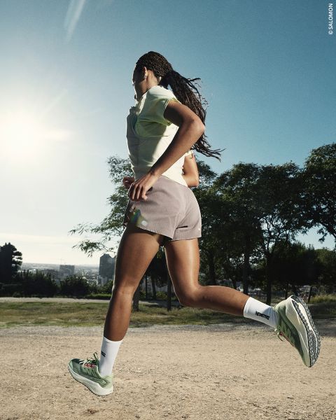 Eine Frau in Sportkleidung läuft im Freien auf einem Feldweg, mit Bäumen und einer hellen Sonne im Hintergrund.