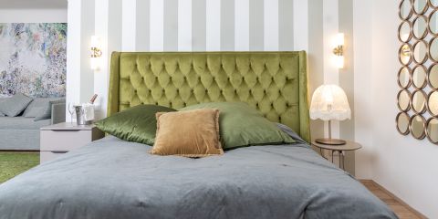 Ein modernes Schlafzimmer mit einem grünen getufteten Kopfteil, grauer Bettwäsche, grünen und goldenen Kissen, Wandlampen und Beistelltischen mit einer Lampe und Dekoration.