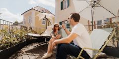 Ein Mann und eine Frau entspannen und unterhalten sich auf einer sonnigen Terrasse mit Liegestühlen, Pflanzen und Sonnenschirmen und genießen die angenehme Atmosphäre im Freien.