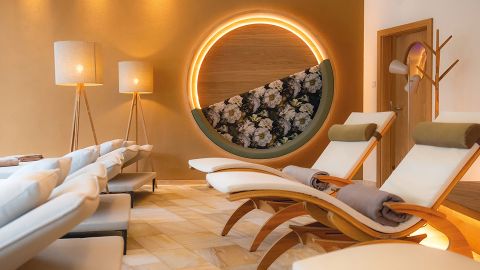 Moderne Spa-Lounge mit gepolsterten Liegestühlen, Stehlampen und einer runden Blumenwand mit warmer Umgebungsbeleuchtung.