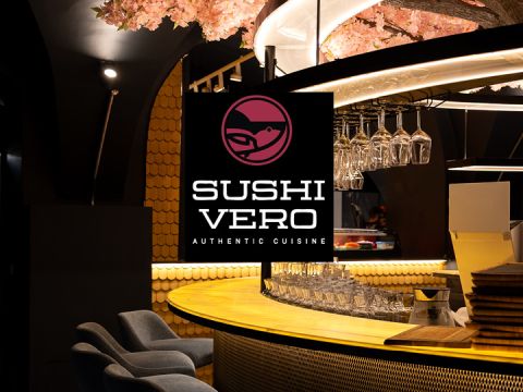 Moderne Sushi-Bar mit rosa Kirschblüten-Dekor, hängenden Gläsern und einem großen Schild mit der Aufschrift "Sushi Vero Authentic Cuisine".
