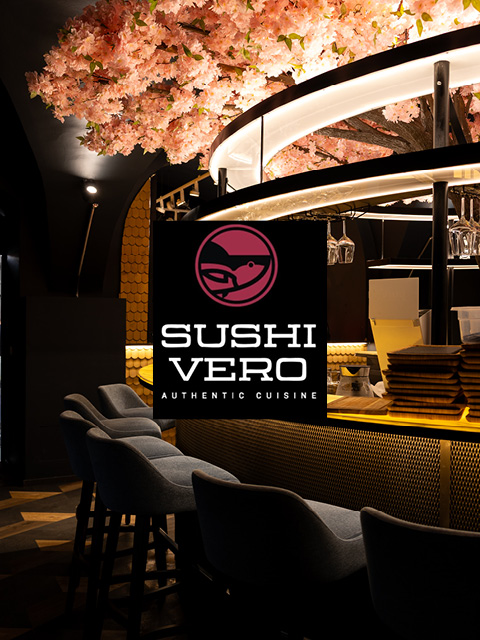Moderne Sushi-Bar mit einem Kirschblütenbaum, stilvollen Sitzgelegenheiten und einer leuchtenden Bar; das Logo von Sushi Vero Authentic Cuisine ist im Bild zentriert.