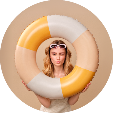 Frau mit langen blonden Haaren und Sonnenbrille, die ein Kussgesicht durch einen gelben und weißen aufblasbaren Schwimmring vor einem beigen Hintergrund macht.