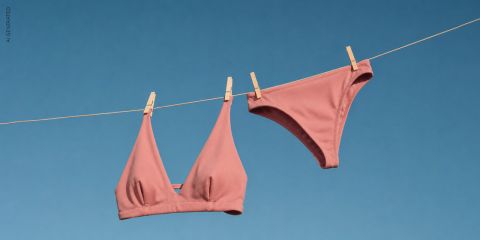 Ein rosa Bikini-Oberteil und -Höschen hängen mit Wäscheklammern an einer Wäscheleine vor einem strahlend blauen Himmel.