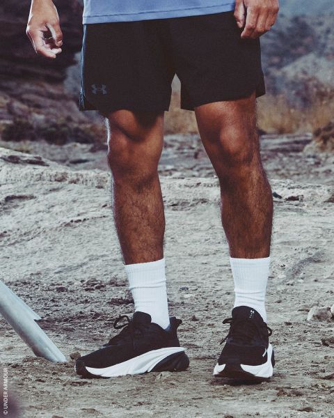 Eine Person in schwarzen Shorts, weißen Socken und schwarzen Turnschuhen steht auf einem felsigen Wanderweg im Freien.