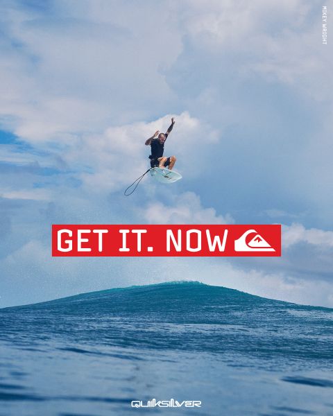 Ein Surfer springt unter blauem Himmel hoch über eine Welle. Der fettgedruckte rote Text lautet "GET IT. NOW", darunter das Quiksilver Logo.
