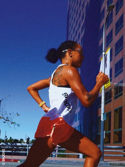 Eine Frau in Sportkleidung läuft unter strahlend blauem Himmel auf einer Stadtstraße neben einem hohen Glasgebäude.