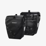 Zwei schwarze Ortlieb-Fahrradtaschen, von vorne und von hinten gezeigt, mit reflektierenden Einsätzen und sicherer Befestigungsvorrichtung vor einem weißen Hintergrund.