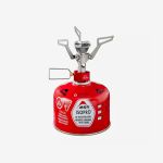Eine rote MSR-Isopro-Gasflasche, auf der ein kleiner silberner Campingkocher befestigt ist, zum Kochen im Freien.