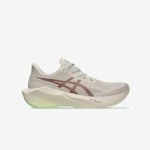 Ein beiger Laufschuh mit einem roten Asics-Logo, einer dicken Sohle und einem Hauch von Hellgrün an der Unterseite, dargestellt vor einem schlichten weißen Hintergrund.