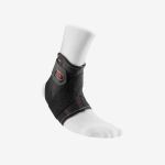 Ein Fuß in einer weißen Socke, an dem eine schwarze Knöchelbandage mit roten Nähten sitzt, die mit verstellbaren Riemen befestigt ist, vor einem schlichten weißen Hintergrund.