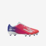 Roter und blauer Fußballschuh mit weißen Schnürsenkeln und Stollen, mit dem SKX-Logo an der Seite vor einem einfarbigen weißen Hintergrund.