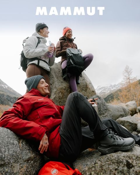 Drei Personen in Outdoor-Kleidung entspannen sich auf Felsen in einer Berglandschaft, über ihnen steht das Wort „MAMMUT“.