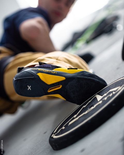 Ein Kletterer, der sich mit mit Magnesia bestäubten Händen und in Kletterschuhen an einer Felswand festhält.