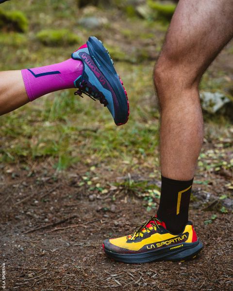 Zwei Beine in Trailrunning-Schuhen und Sportsocken, die auf einem Feldweg stehen.